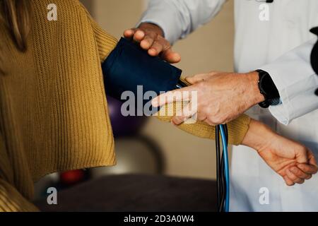 Male doctor removing blood pressure machine from female arm during checkup in doctors office. Stock Photo