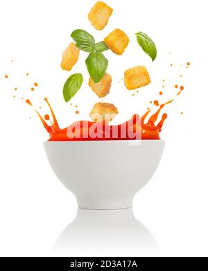 basil leaves and croutons falling into a tomato soup bowl isolated on white Stock Photo