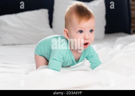 selective focus of infant boy in baby romper crawling in bed with open mouth Stock Photo