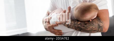 selective focus of tattooed man holding baby boy, horizontal concept Stock Photo