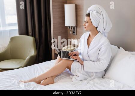 barefoot young freelancer in bathrobe using laptop on bed Stock Photo