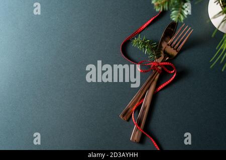 Christmas or new year table setting with golden cutlery and red bow, decorated with natural pine branches, on dark green background Stock Photo