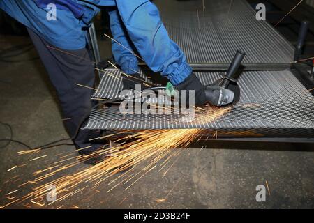 A worker cuts an iron mesh netting with an iron circle. Sparks fly Stock Photo