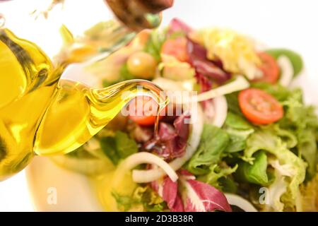 Pouring olive oil from glass oil dispenser on salad plate. Top view. Stock Photo