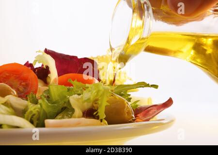 Pouring olive oil from oil dispenser over prepared salad on white plate and isolated background Stock Photo