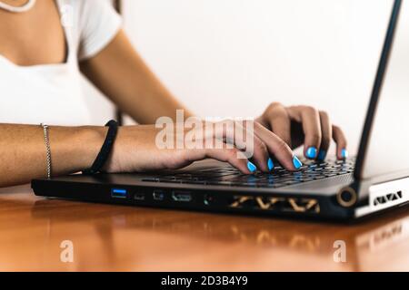 Closeup of a girl's hands typing on a black laptop on a wooden table Stock Photo