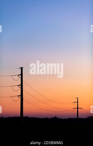 Silhouette of power lines over colorful clear sky at sunrise or sunset, blackout concept. Stock Photo