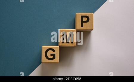 Wood cubes with word 'GMP, good manufacturing practice' stacking as step stair on paper blue and white background, copy space. Business concept. Stock Photo
