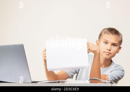 Kid hands holding open notebook with blank white pages Boy sitting at table with books and laptop computer Stock Photo