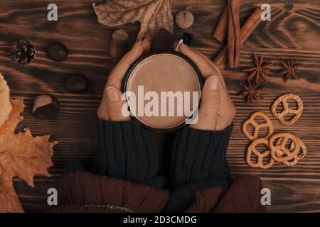 Top view composition with young woman's hands in red blue sweater, vintage styled cup of hot chocolate and  decoration from fall leaves, acorns Stock Photo