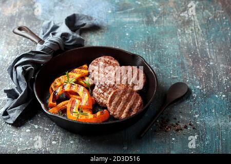 Beef patties for burger with grilled pumpkin in a cast iron pan, selective focus Stock Photo