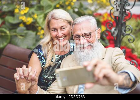 Happy senior couple taking selfie with mobile smart phone outdoor - Mature retired people having fun with new technology social media apps Stock Photo