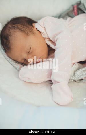 Caucasian newborn girl sleeping in pink clothes lying on a soft white blanket Stock Photo