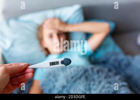 Sick teenage little girl with high fever and headache laying in bed. Stay at home during corona virus epidemic if you feel sick Stock Photo