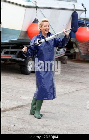 White Caucasian dyed blonde middle aged woman in her 40s wearing a blue shiny PVC raincoat purchased from a second hand shop. Pretending to dance in her raincoat and wellington with an umbrella Stock Photo