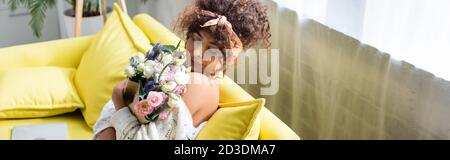 horizontal image of young woman with closed eyes holding bouquet and smelling flowers in living room Stock Photo