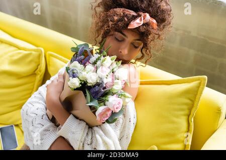 young woman with closed eyes holding bouquet and smelling flowers in living room Stock Photo
