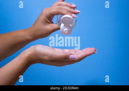 Caucasian woman using bottle with antibacterial antiseptic gel in hand, close up with blue background Stock Photo