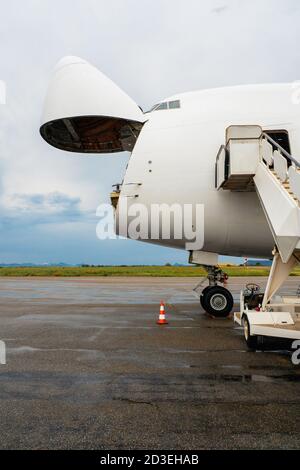 A Jumbo Jet freighter aircraft with a wide open nose cargo door waiting at a cargo ramp for a high-loader to be offloaded Stock Photo