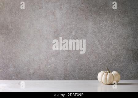 White whole uncooked decorative pumpkin on white marble table with grey wall at background. Autumn minimalist decoration. Stock Photo