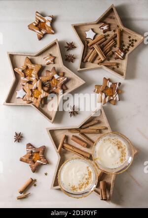 Eggnog Christmas milk cocktail, served in two vintage crystal glasses on wooden tray with shortbread star shape sugar cookies, cinnamon sticks over wh Stock Photo