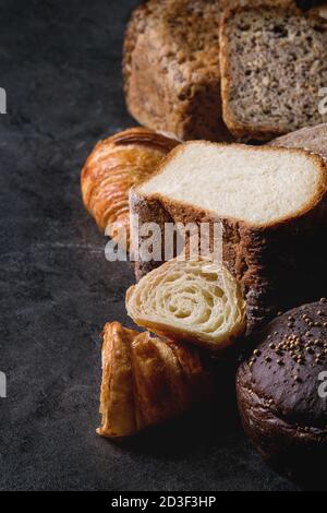 Variety of fresh baked rye, spelled, wheat craft artisan bread, whole and sliced, on black texture background. Close up Stock Photo