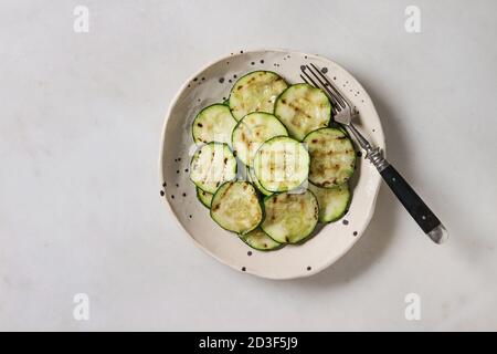 Grilled zucchini salad in spotted ceramic plate with vintage fork over white marble background. Vegan food. Flat lay, space Stock Photo