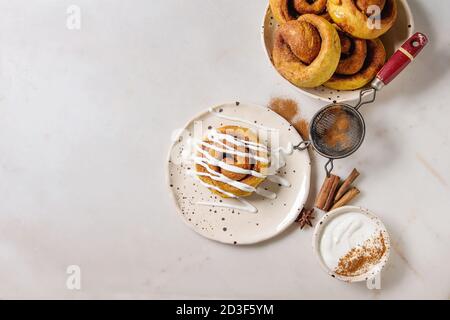 Homemade pumpkin cinnamon bun rolls sweet autumn baked dessert with cream cheese sauce in spotted ceramic plates with cinnamon sticks and vintage siev Stock Photo