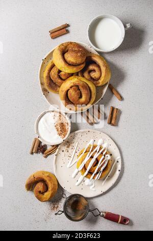 Homemade pumpkin cinnamon bun rolls sweet autumn baked dessert with cream cheese sauce in spotted ceramic plates with cinnamon sticks and vintage siev Stock Photo