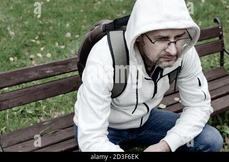 A middle-aged man in a hooded sweater sitting alone on a park bench Stock Photo