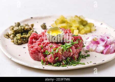 Beef tartare with quail egg in shell, cutting pickled cucumbers, capers, red onion, chives and arugula salad served in spotted ceramic plates with pep Stock Photo