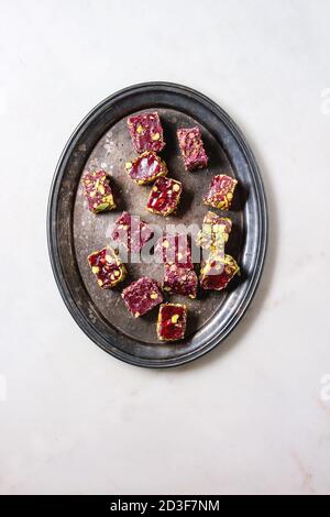 Variety of traditional turkish dessert Turkish Delight different taste and colors with rose petals and pistachio nuts on vintage tray over white marbl Stock Photo