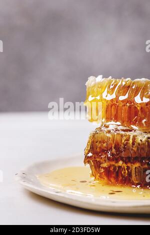 Stack of organic honey in honeycombs in spotted ceramic plate on white marble table. Stock Photo