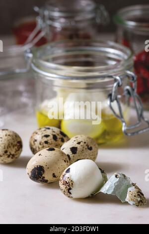 Ingredients for homemade pickled marinated quail eggs. Boiled eggs with olive oil in jar on white marble kitchen table. Close up Stock Photo