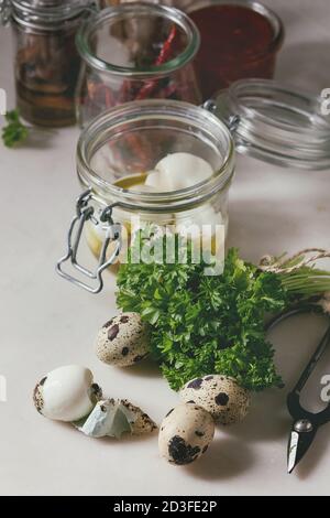 Ingredients for homemade pickled marinated quail eggs. Eggs in plastic box, tomato sauce, chili peppers, anchovies in jars, fresh greens, scissors, ol Stock Photo