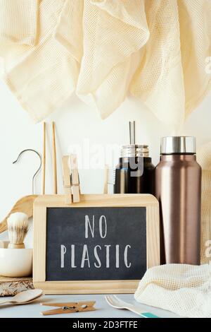 the text no plastic in a chalkboard and a pile of no-plastic sustainable items, such as metal water bottles, a glass bottle, shopping mesh bags or reu Stock Photo