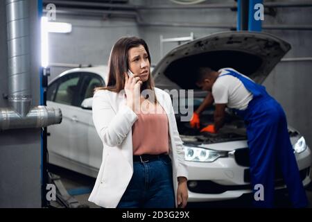A woman is talking on the phone. Repairer in the background fixing a car Stock Photo