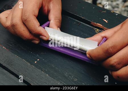 Man hand makes a cigarette with rolling traditional tools, hands closeup. Stock Photo