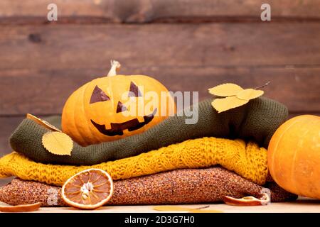 Stack of winter sweaters and Halloween pumpkin head jack lantern on wooden background Stock Photo