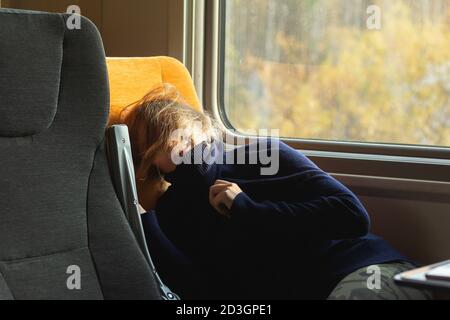 Young woman traveler sleeping inside of suburban train. She covered her face with a sweater. Stock Photo