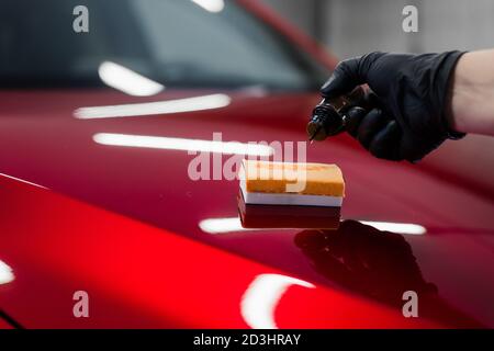 Car detailing - Man applies nano protective coating or wax on red car. Covering car bonnet with a liquid glass polish. Stock Photo