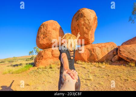 Hand in hand couple at Devils Marbles, Northern Territory: the Eggs of mythical Rainbow Serpent. Follow me, tourist woman at iconic landscape of Stock Photo