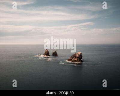 Minimalist landscape of three lonely rocks in the sea. Los Urros, Liencres, Cantabria, Spain. Stock Photo