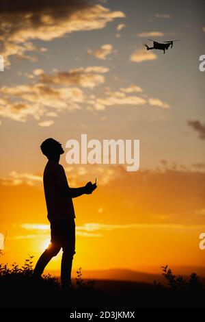 Silhouette of a young man operating a drone in A Rural Setting on sunset Stock Photo