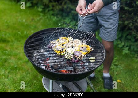 A young male grilling preparing vegetables over a charcoal grill to get a smoky flavour for a healthy party dinner Stock Photo