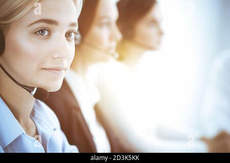 Call center and business people concept. Beautiful business woman with headphones consulting clients. Group of diverse phone operators at work in Stock Photo
