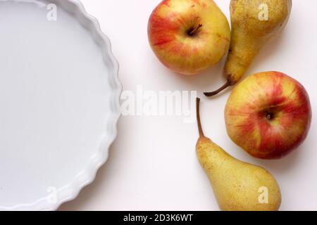 Empty white ceramics tart or pie baking dish, on white table, with fresh apples and pears; with copy space Stock Photo