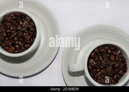 Coffee beans in two coffee cups , on white isolated background.Top view.Macro. Stock Photo