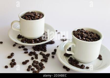 Roasted coffee beans in two coffee cups , on white isolated background. Stock Photo