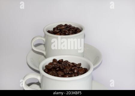 Roasted coffee beans in two coffee cups , on white isolated background. Stock Photo